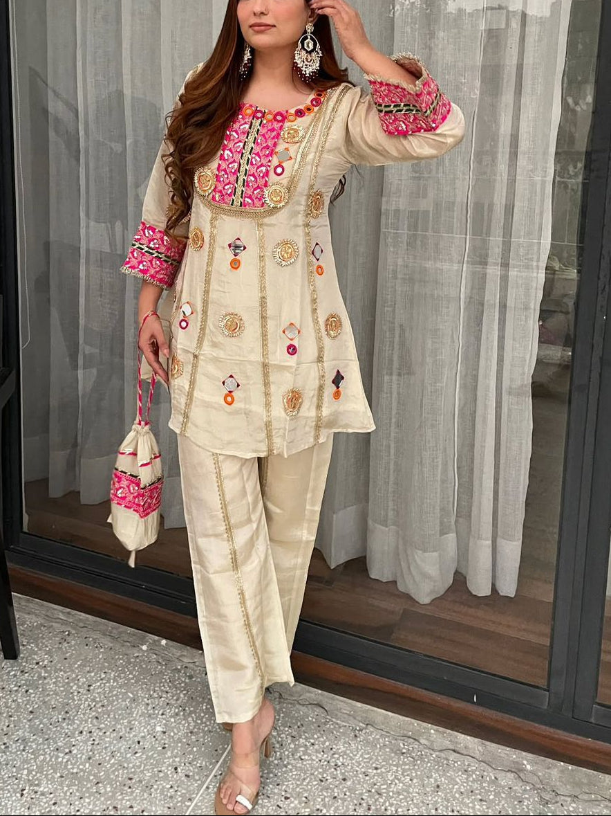 Woman in traditional embroidered outfit standing in a modern indoor setting.