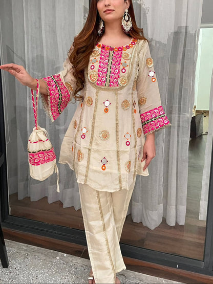 Woman in traditional outfit with pink and gold embroidery, holding a matching bag.