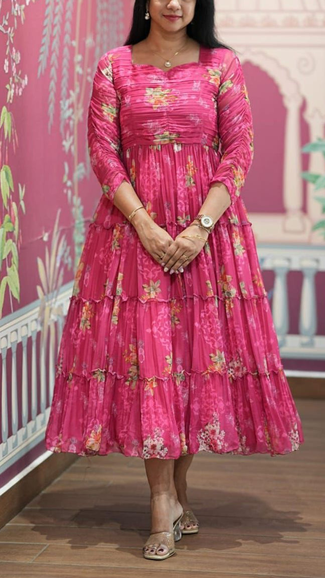 Woman in a pink floral dress standing against a decorative pink wall.