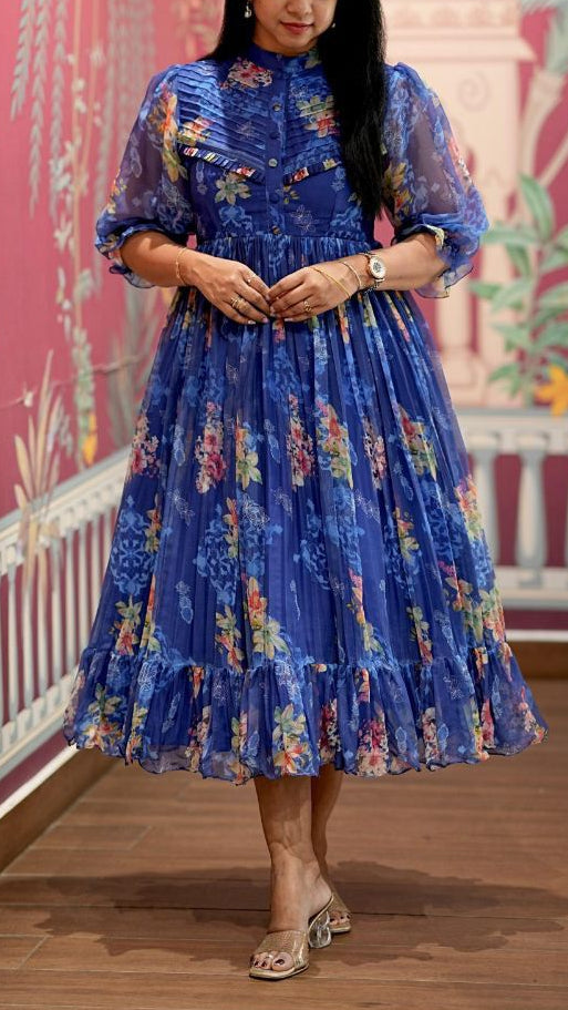 Woman in a blue floral dress standing in front of a decorative wall with pink and green patterns.