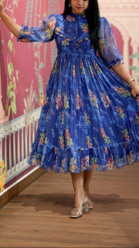 Woman in a blue floral dress standing in front of a decorative wall.