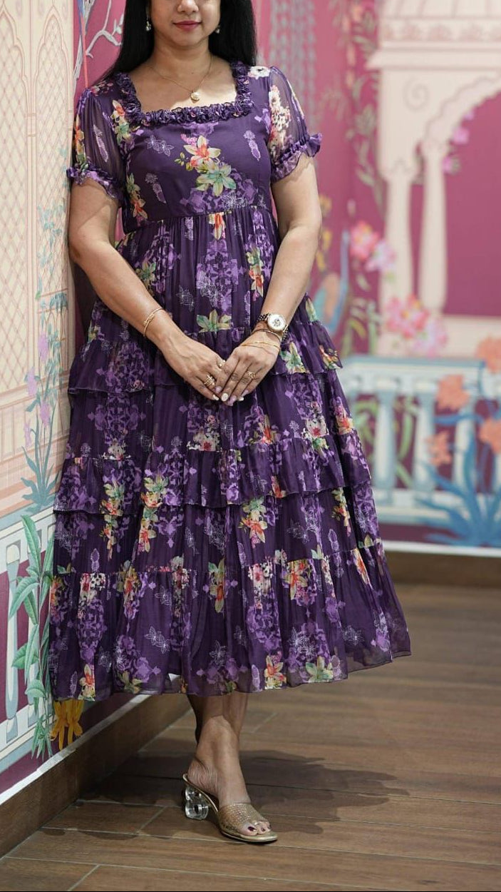 Woman in a purple floral dress standing in front of a colorful wall with architectural designs.