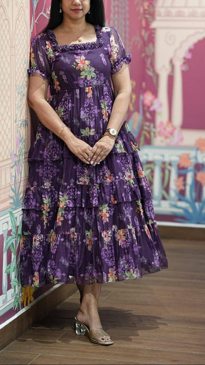 Woman in a purple floral dress standing in front of a colorful wall with architectural designs.