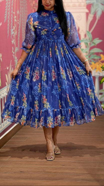Woman wearing a blue floral dress standing in front of a decorative wall.