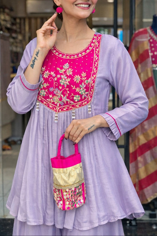 Woman wearing a light purple traditional outfit with pink embroidery, holding a matching handbag in a store setting.