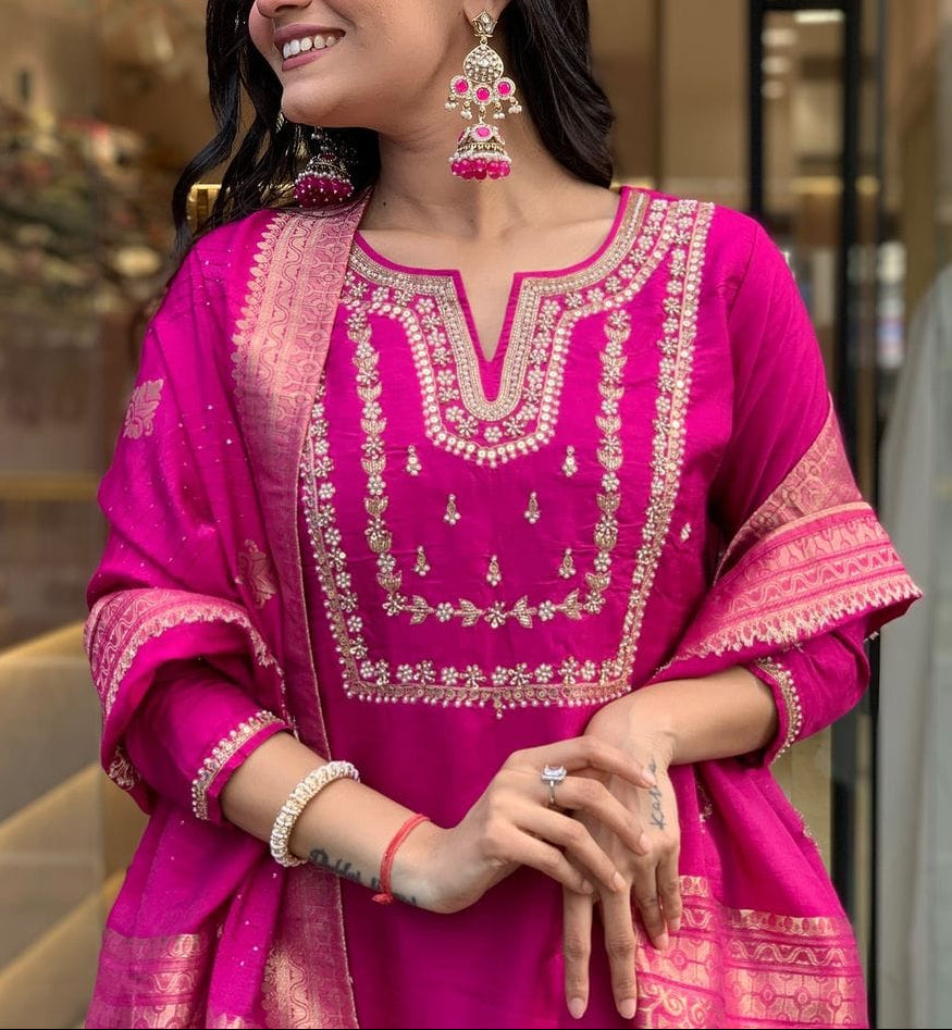 Woman in a pink traditional outfit with gold embroidery, standing indoors.