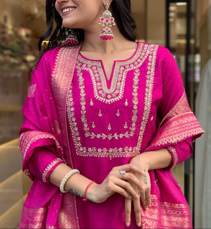Woman in a pink traditional outfit with gold embroidery, standing indoors.